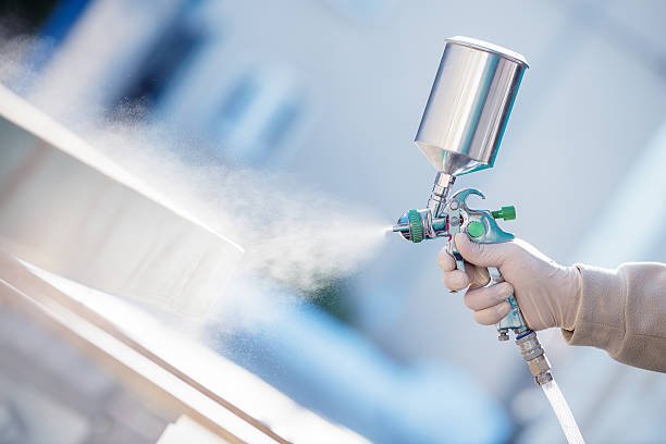 Hand holding a spray gun and painting wood in furniture factory.