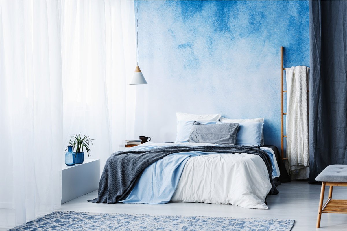 a modern bedroom with the wall behind the bed painted with a blue ombre pattern